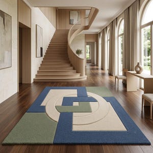 May include: A rectangular area rug featuring a geometric pattern of interlocking blue, sage green, and cream-coloured shapes. The design includes a central circular motif surrounded by angular blocks and lines, creating a textured surface.