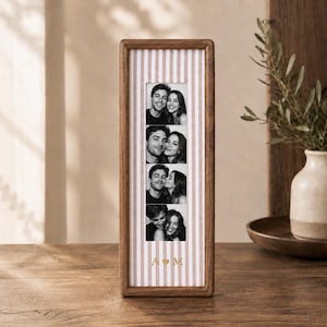 May include: A tall, rectangular wooden picture frame featuring a vertical strip of four black and white photographs of a couple. The frame has a light pink and white striped matting with the gold letters A and M separated by a heart symbol.