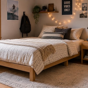 May include: A wooden bed frame with a white and black patterned duvet cover, a beige throw blanket, and several pillows. The bed is positioned next to a wooden nightstand with a black lamp, and a guitar stands nearby on a light-colored rug.