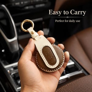 May include: A round brown leather car key fob cover with white stitching and a cream-colored leather strap attached to a gold-toned metal ring. The text "Easy to Carry" and "Perfect for daily use" is visible in the upper right corner of the image.