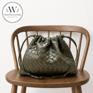 Può includere: Una borsa a sacchetto color verde oliva con una texture intrecciata simile alla pelle. La borsa presenta una chiusura arricciata nella parte superiore con due sottili cinturini laterali abbinati. Un logo circolare riporta WearTheoryFinds FIND YOUR STYLE.