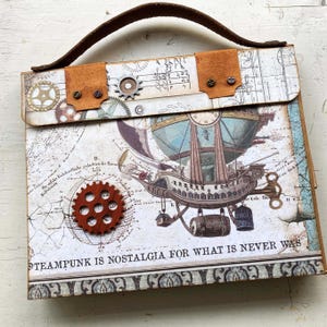 May include: A brown leather-handled box with a steampunk design. The box features a vintage map, a hot air balloon, and gears. The text "STEAMPUNK IS NOSTALGIA FOR WHAT IS NEVER WAS" is printed on the front of the box.