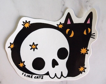 Könnte beinhalten: Schwarz-weißer Aufkleber eines Katers mit einem Schädel als Kopf. Die Katze hat rosa Ohren und gelbe Augen. Der Aufkleber hat einen weißen Hintergrund mit gelben Sternen und dem Text "Ich mag Katzen".