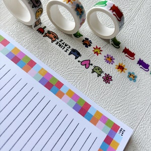 Peut inclure: Quatre rouleaux de ruban adh&eacute;sif washi color&eacute; avec des motifs de chats et de fleurs. Le ruban est sur une surface blanche avec un bloc-notes lign&eacute; avec une bordure color&eacute;e qui dit "J'aime les chats".
