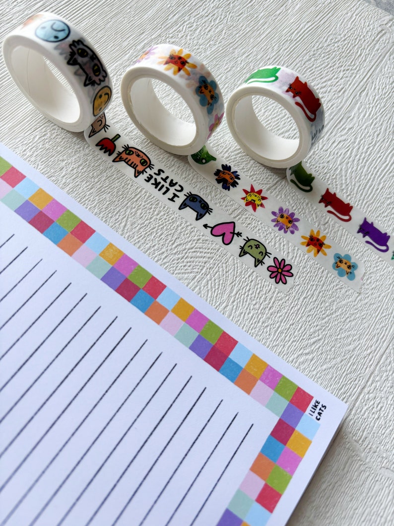 Peut inclure: Quatre rouleaux de ruban adh&eacute;sif washi color&eacute; avec des motifs de chats et de fleurs. Le ruban est sur une surface blanche avec un bloc-notes lign&eacute; avec une bordure color&eacute;e qui dit "J'aime les chats".