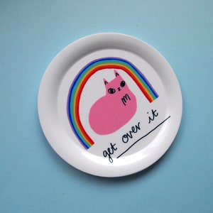 May include: White ceramic plate featuring a pink cat sitting on a rainbow with the text "get over it".