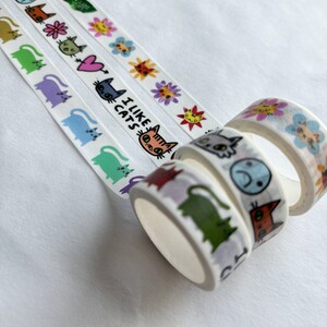 Peut inclure: Quatre rouleaux de ruban adh&eacute;sif washi color&eacute; avec des motifs de chats. Le ruban pr&eacute;sente des chats avec diff&eacute;rentes expressions, notamment un c&oelig;ur, un poisson et les mots "J'aime les chats".