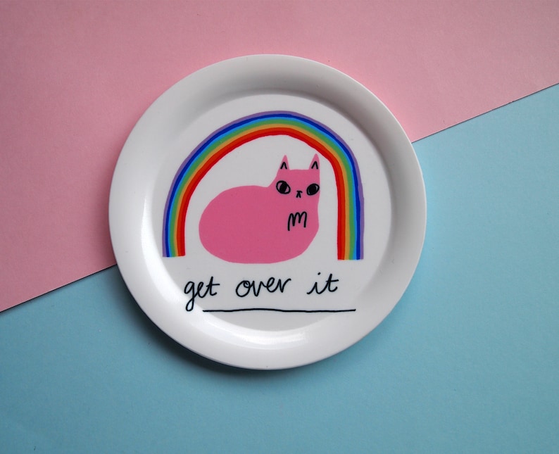May include: White ceramic plate featuring a pink cat lying under a rainbow with the text "get over it".