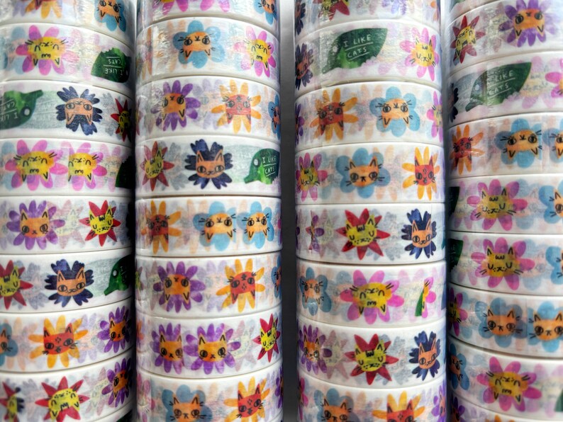 Peut inclure: Rouleaux de ruban adh&eacute;sif washi color&eacute; avec un motif r&eacute;p&eacute;titif de chats et de fleurs. Le ruban porte l'inscription "J'aime les chats".