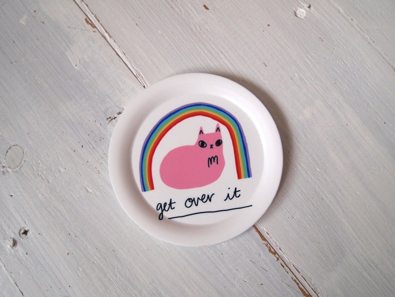 May include: White ceramic plate featuring a pink cat sitting under a rainbow with the text "get over it".