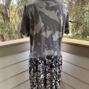 May include: A short-sleeved shirt featuring a charcoal grey and light grey acid-wash pattern on the upper portion, with a contrasting black and white floral print fabric attached at the waist, creating a layered, dress-like appearance.