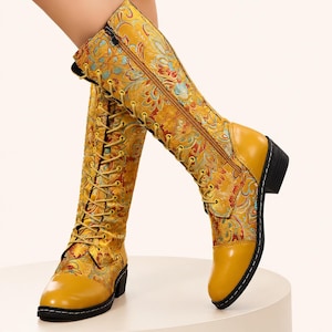 May include: Knee-high boots featuring a vibrant yellow, orange, and teal floral brocade fabric upper. These boots include a solid yellow toe cap, a full-length side zip, and yellow laces that run up the front, finished with a low black heel.
