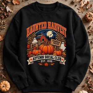 Peut inclure: Un sweat-shirt noir à col rond avec une impression graphique portant le texte HAUNTED HARVEST, PUMPKIN PATCH et AUTUMN SOCIAL CLUB EST. 1998. Le motif montre des citrouilles orange, une grange rouge, deux fantômes blancs et une pleine lune.
