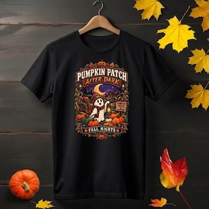 Peut inclure: Un t-shirt noir à manches courtes avec une impression graphique représentant un fantôme portant un chapeau et une écharpe, tenant une lanterne dans un champ de citrouilles. Le texte indique PUMPKIN PATCH AFTER DARK et FALL NIGHTS.
