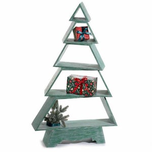 Puede incluir: Una estantería de madera en forma de árbol con varios niveles y un acabado verde desgastado. La estructura tiene cuatro niveles horizontales de diferentes anchos. Un regalo pequeño con lazo azul, uno más grande con lazo rojo y una rama de pino.