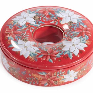 Pode incluir: Uma lata metálica redonda vermelha com um orifício central, apresentando um padrão decorativo de flores de poinsétia brancas e vermelhas, folhas de azevinho verdes, pinhas e pequenas bagas vermelhas dispostas em coroa no topo e nas laterais.