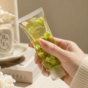 May include: A clear, flexible squeeze tube filled with a translucent yellow gel containing small, light green flower-shaped embellishments. The tube features the white text "Chibok" printed on the front surface and has a clear plastic cap.