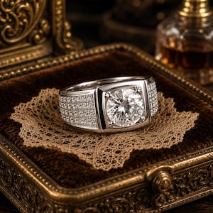 May include: A silver-toned ring featuring a large, round, brilliant-cut clear stone set in a square-shaped bezel. The wide band is encrusted with multiple rows of small, sparkling clear stones that extend along the sides of the ring.