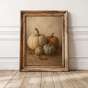 May include: A framed wall art print featuring a still life painting of four pumpkins in varying shades of cream, orange, and muted green, arranged on a textured surface with scattered dried autumn leaves, enclosed in a weathered wooden frame.