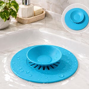 May include: A bright blue circular sink stopper and hair catcher featuring a central suction cup handle and a series of radial drainage slots. The flexible silicone disc is shown resting flat over a drain, with a circular inset view above.