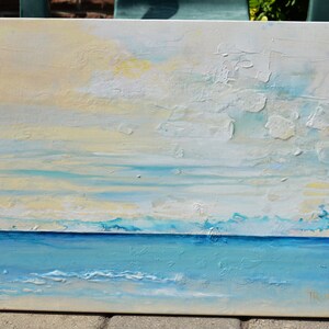 May include: Abstract painting of a seascape with a blue ocean and a white and yellow sky. The painting has a textured surface and is signed "Trudie".