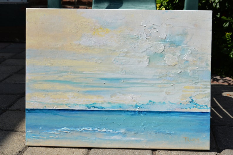 May include: Abstract painting of a seascape with a blue ocean and a white and yellow sky. The painting has a textured surface and is signed "Trudie".
