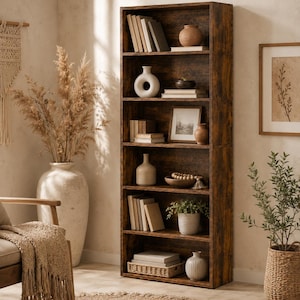 May include: A tall, six-shelf bookcase with a dark, distressed wood grain finish. The shelves are filled with various items including stacks of books, ceramic vases in neutral tones, a framed picture, a small potted plant, and a woven basket.
