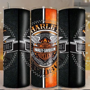 Peut inclure: Un gobelet cylindrique avec un fond noir à texture de cuir et une bande verticale orange centrale. Le motif comprend le logo Harley-Davidson, des ailes et le texte "Ride", "To Live", "Live To Ride" et "Since 1903" en blanc et orange.