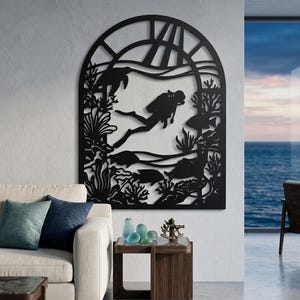 May include: A black metal wall art piece featuring an arched frame with a laser-cut design of an underwater scene. The silhouette depicts a scuba diver swimming among coral reefs, sea plants, a sea turtle, and various fish within the frame.