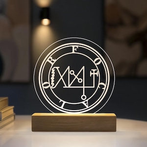 Pode incluir: Um expositor de luz circular em acrílico transparente com o selo gravado em branco de Focalor rodeado pelas letras F, O, C, A, L, O, R. O disco de acrílico está montado numa base retangular de madeira que ilumina o design.