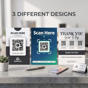 May include: Three rectangular payment signs with QR codes. The left sign is black and white with the text SCAN HERE. The middle sign is blue and green with the text Scan Here. The right sign is white with black text THANK YOU SCAN TO PAY.