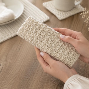 May include: A rectangular, cream-colored crochet sleeve featuring a dense, textured stitch pattern. The item is constructed from yarn and has a uniform, woven appearance throughout its surface, showcasing a consistent handmade construction style.
