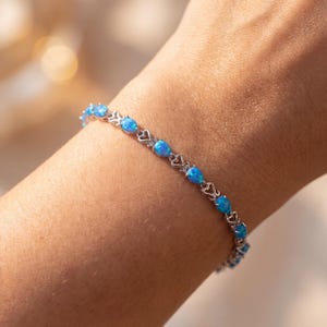May include: A silver-toned bracelet featuring a series of pear-shaped, vibrant blue opal stones. Each stone is separated by a delicate, openwork metal link design that connects the individual settings in a continuous, repeating pattern.