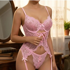 May include: A light pink lace bodysuit featuring a floral pattern, underwire cups, thin adjustable shoulder straps, a lace-up front detail, and attached garter straps. The garment is constructed from sheer floral lace with scalloped edges.