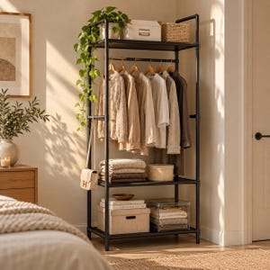 May include: A black metal garment rack with four shelves and a hanging rod. The top shelf holds a potted trailing plant, a white box, and a woven basket. Clothes hang on wooden hangers, while folded textiles and storage boxes sit on lower shelves.