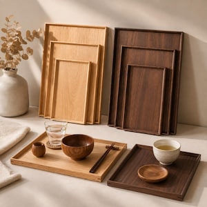 Puede incluir: Una colección de bandejas de servicio rectangulares de madera en acabados claros y oscuros, presentadas en juegos encajables. El conjunto incluye bandejas planas, un cuenco de madera pequeño, un vaso de agua, palillos y una taza de té.