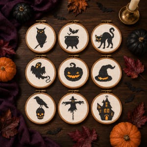 May include: Nine circular wooden embroidery hoops containing cross-stitch designs on white fabric. The patterns feature black and orange Halloween motifs including an owl, a cauldron, a cat, a ghost, a jack-o'-lantern, a witch hat, a crow on a skull, a scarecrow, and a haunted house.