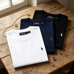 Peut inclure: Trois t-shirts à col rond en blanc, bleu marine et noir, chacun doté d'une étiquette Polo Ralph Lauren à l'intérieur du col et d'un petit logo poney brodé sur la poitrine. Le t-shirt blanc a un logo sombre, le bleu marine un logo rouge et le noir un logo blanc.