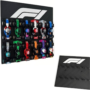 May include: A black wall-mounted display board featuring a white F1 logo at the top, designed to hold twelve miniature Formula 1 race cars. The display includes a second, smaller empty black board with the same white F1 logo and mounting slots.