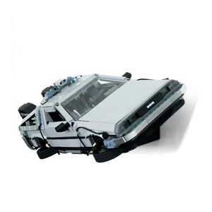 May include: A light gray building block model of a sports car featuring a wedge-shaped body, black tires, and a front grille with the text DMC. The vehicle includes intricate mechanical details on the roof and rear, with a transparent windshield.
