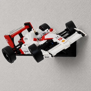 May include: A white, red, and black plastic building block model of a Formula 1 race car. The car features the number 12, Honda and Shell branding, and a McLaren logo on the front wing. It is mounted horizontally on a wall-mounted display bracket.