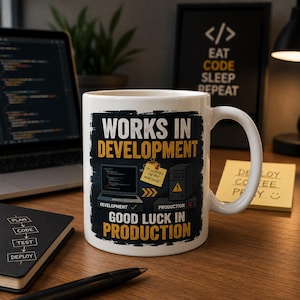 May include: A white ceramic mug featuring a graphic with the text "WORKS IN DEVELOPMENT" and "GOOD LUCK IN PRODUCTION." The design includes a laptop, a server icon, and a yellow sticky note that reads "IT WORKED ON MY MACHINE" with arrows.