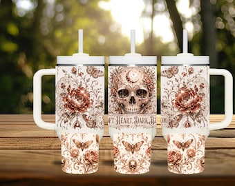 May include: A white tumbler with a handle and straw featuring a copper-toned design of a skull, crescent moon, blooming flowers, and moths. The text "SOFT HEART, DARK BLOOM" is printed across the center of the intricate, vintage-style pattern.