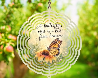 May include: A circular metal wind spinner featuring a monarch butterfly perched on a yellow flower. The center includes the text A butterfly visit is a kiss from heaven in black script. The outer edge has a scalloped, layered metal design.
