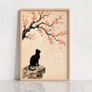 May include: A framed wall art print featuring a black cat sitting on a rock, looking up at a sprawling tree branch with light pink cherry blossoms. The background is a soft cream color with scattered falling petals in a watercolor style.