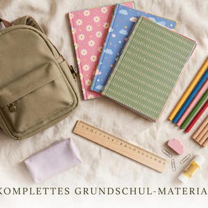 May include: An olive green backpack, three notebooks with floral, cloud, and dash patterns, a wooden ruler, colored pencils, a light purple pencil case, a pink cloud-shaped eraser, two paper clips, and a glue stick with text KOMPLETTES GRUNDSCHUL-MATERIAL.