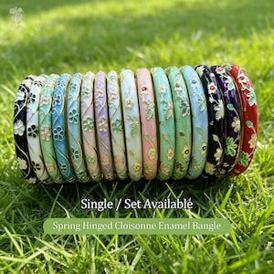 Puede incluir: Una colección de quince brazaletes con bisagras que presentan superficies de esmalte de colores con patrones de enredaderas florales en tono dorado. Las pulseras están dispuestas en fila e incluyen variaciones de color negro, blanco, verde claro, azul, rosa, lavanda y rojo.