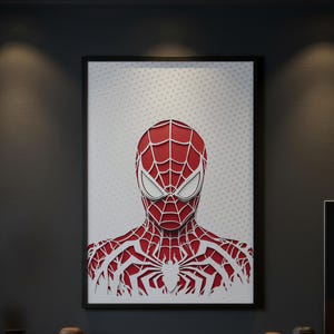 Op de afbeelding: Een ingelijste kunstdruk met een illustratie van Spider-Man in een gelaagde papierknipselstijl. Het personage is afgebeeld in rood met witte webpatronen en witte ogen op een lichtgrijze achtergrond met een subtiel wit stippenpatroon.