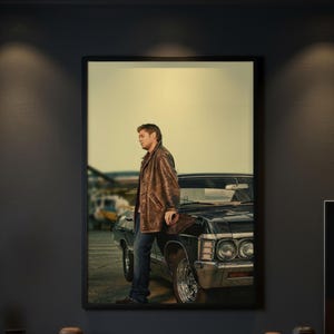 Può includere: Una stampa artistica da parete incorniciata raffigurante una persona con capelli castani corti che indossa una giacca di pelle marrone e jeans blu, appoggiata al parafango anteriore di un'auto nera d'epoca.