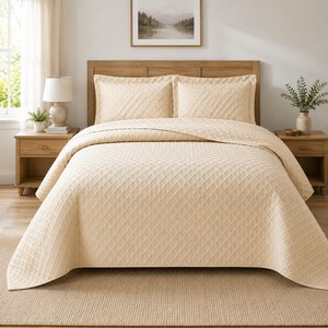 May include: A light beige bedspread and two matching pillow shams featuring a repeating embossed geometric wave pattern. The bedding set is draped over a bed with a wooden headboard, creating a uniform and textured appearance across the surface.